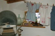 Waschküche mit alter Badewanne und Wäschemangel, auf einer Wäscheleine alte Kinderkleidung aufgehängt.